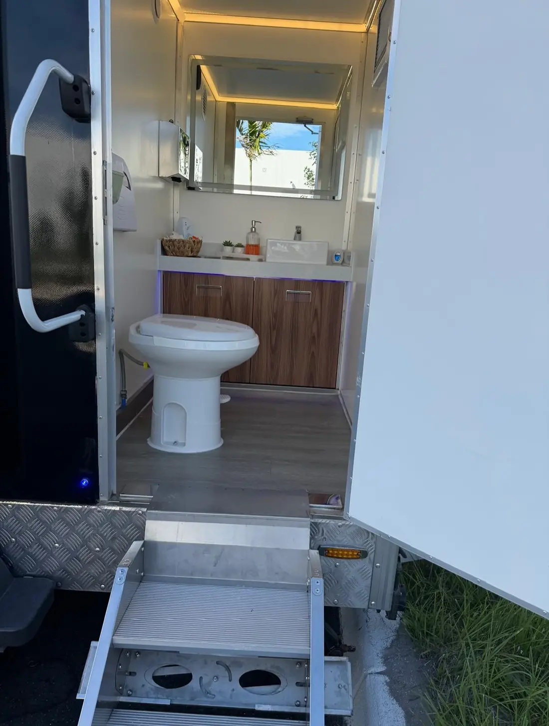 Restroom trailer stall with flushing toilet and wood vanity sink