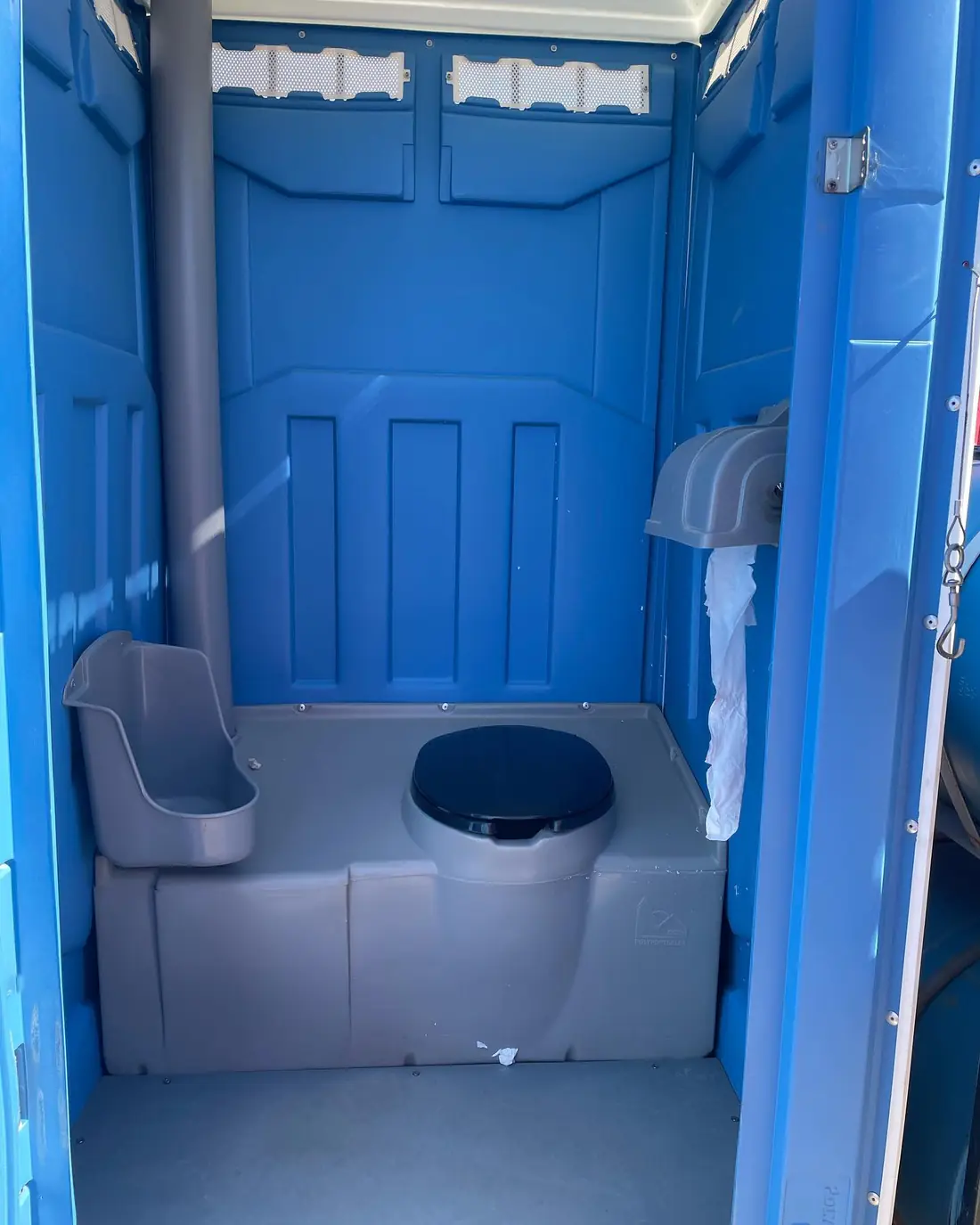 Inside a blue standard porta potty showing toilet seat, urinal and paper holder