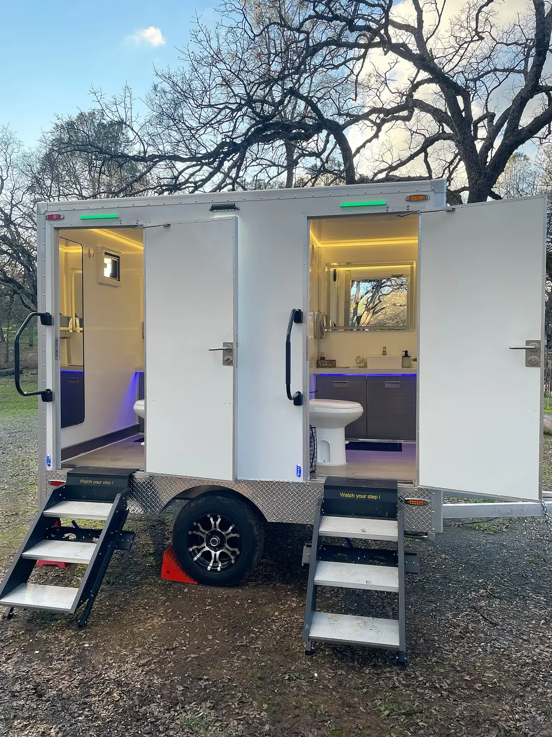 Two-stall restroom trailer with lit interiors parked on gravel